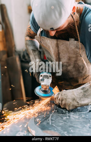 Axe maker using steel grinder in workshop