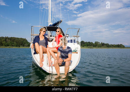 Young man and adult women sitting chatting on sailboat on Chiemsee lake, Bavaria, Germany Stock Photo