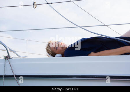 Mature woman sunbathing on sailboat on Chiemsee lake, portrait, Bavaria, Germany Stock Photo