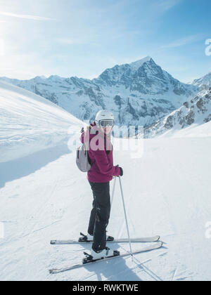 Young woman skier wearing helmet and ski goggles looking back in snow covered landscape,  Alpe Ciamporino, Piemonte, Italy Stock Photo