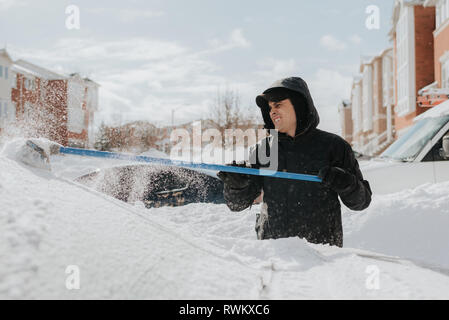 Man clearing snow-covered vehicle with broom, Toronto, Canada Stock Photo