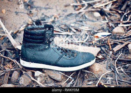 Dumped single wet black boot standing on muddy soil surface Stock Photo