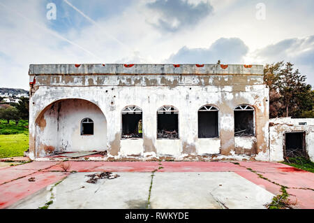 Exterior of an abandoned old white concrete single story house in a rural meadow field. Stock Photo