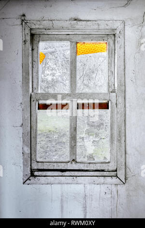 Interior of a ruined house with old, dirty and cracked white wall and vintage wooden window frame with broken glass Stock Photo