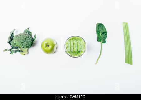 Creative flat lay composition of glass of green smoothie next to ingredients: broccoli, apple, spinach leaf and celery stalk on white background, top  Stock Photo