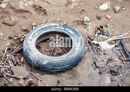 Dumped worn wet car tire on muddy soil ground Stock Photo