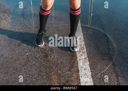 From above crop legs of young lady in legwarmers and jogging shoes standing in water slops on asphalt Stock Photo