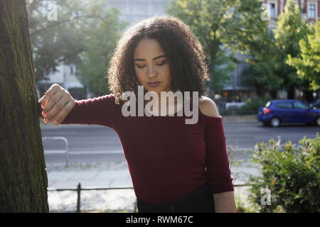 Young woman leaning on tree, Berlin, Germany Stock Photo