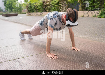 Man in push up position using virtual reality goggles, Berlin, Germany Stock Photo