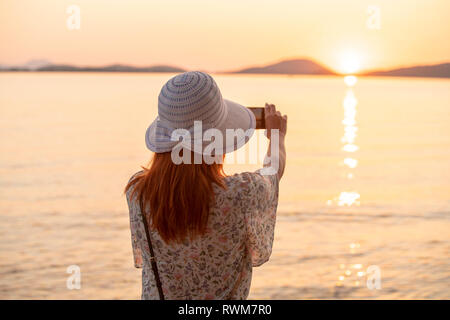 Tourist taking photograph of sunset on beach Stock Photo