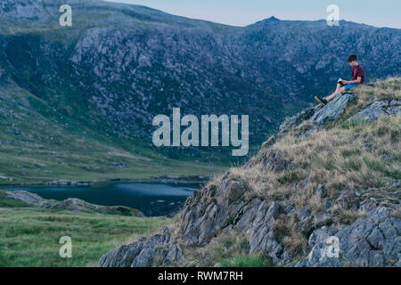 Boy reading book on hilltop, Snowdonia, Llanberis, Gwynedd, UK Stock Photo