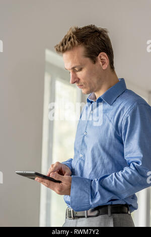 Handsome young businessman standing by the office windows browsing the internet using didgital tablet. Stock Photo
