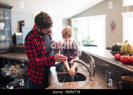 Father watching son wash hands in kitchen sink Stock Photo