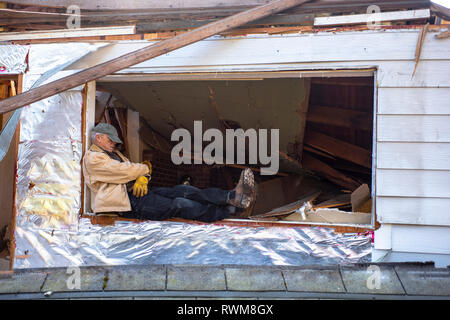 Man snoozing on a worksite, sitting on the ledge of an open window under repair; Olympia, Washington, United States of America Stock Photo