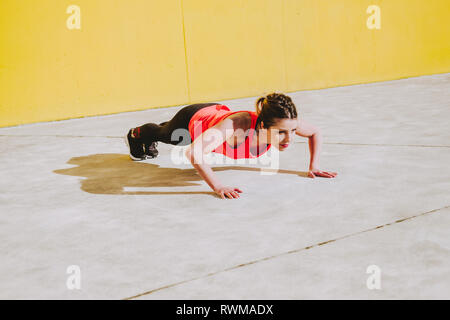 Young lady in sportswear doing planks on floor near yellow wall Stock Photo