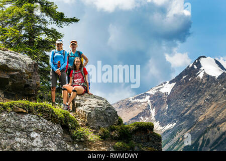 Three female hikers on a mountain rock with mountain and blue sky in the background; British Columbia, Canada Stock Photo