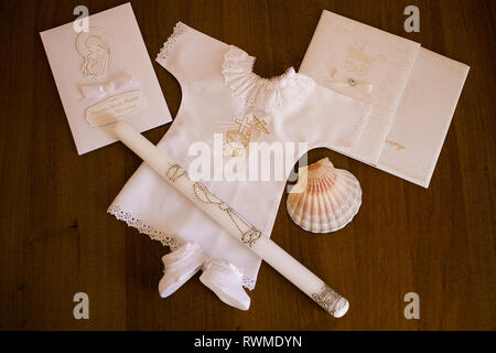 Symbols of Christening a baby in catholic tradition: cloth, candle, seashell for pouring holly water over baby's head and tiny shoes on a brown wooden Stock Photo