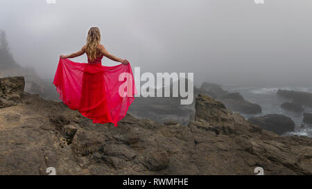 A woman stands on a cliff edge overlooking the angry sea on a foggy late afternoon in State Arago Park, stitched pano composite Stock Photo