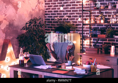Young man watching stream of football match and rejoicing over his favorite team while sipping wine. Stock Photo