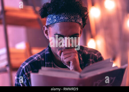 Close up of a young man giggling about something that he finding in the book. Stock Photo