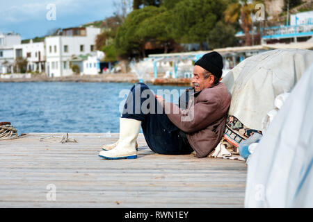 Portrait of an old Turkish fisherman sitting on the dock on a winter day in Bodrum, Gumusluk, Mugla, Turkey. Stock Photo