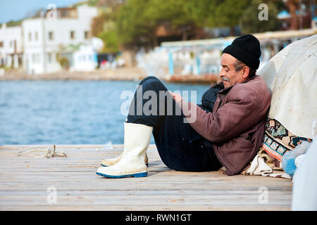 Portrait of an old Turkish fisherman sitting on the dock on a winter day in Bodrum, Gumusluk, Mugla, Turkey. Stock Photo