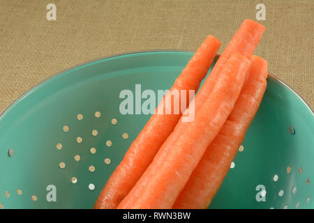 Close up of freshly trimmed and rinsed raw carrots in blue colander Stock Photo