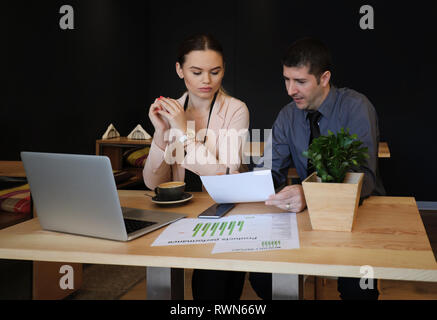 Couple doing accounts in a small cafeteria. Man and woman working on laptop in cafe Stock Photo