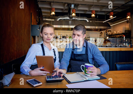 Small family restaurant owners checking monthly reports. Man and woman wearing apron doing accounts for their small restaurant. Stock Photo