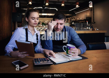 Young entrepreneurs going over documents in the restaurant. On table phone, tablet, cup of coffee, notebook Stock Photo