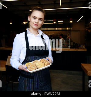 Smiling Young Woman holding fresh parsley. Blurry restaurant counter and employees working in background Stock Photo