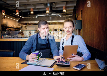 Man and woman wearing apron doing accounts after hours in a small restaurant. Employees checking monthly reports Stock Photo
