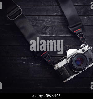 Classic camera on film with a strap. Wood black table background. Low-key light. Space for text Stock Photo