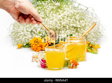 Hand with dipper picking honey from a jar of honey. Jars of honey with flowers on white background. Front view. Horizontal composition Stock Photo