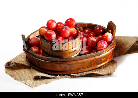 Red Mirabelle plum in basket on white background. Known as mirabelle prune or cherry plum, is a cultivar group of plum trees of the genus Prunus. Stock Photo