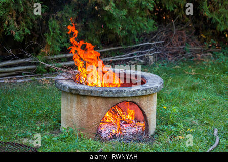 Dry branches burn in isolated campfire pit in the garden. High bright flames flickering on open garden fire pit. Stock Photo