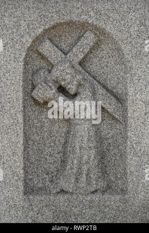 Carved stone figure carrying a cross seen on water fountain outside Church of St Nicolas; La Coruna, Spain Stock Photo