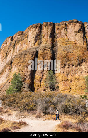 A woman walking on a trail below massive cliffs  in the Pinnacles National Park; California, United States of America Stock Photo