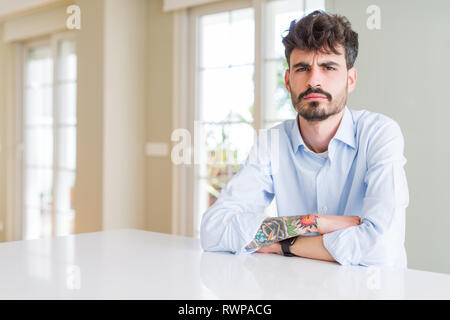 Young businesss man sitting on white table skeptic and nervous, frowning upset because of problem. Negative person. Stock Photo