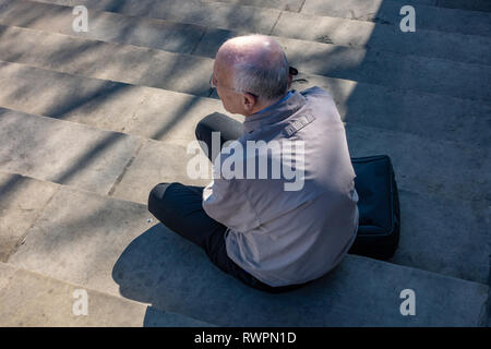 bird's eye view of slim elderly man with grey thinning hair, sitting on step in the sun Stock Photo