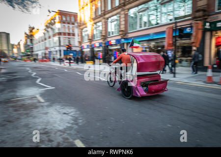 Rickshaw driver on his purple taxi trike, moving through the streets of Central London Stock Photo