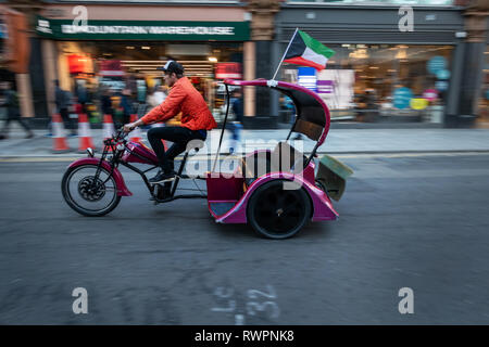 Rickshaw driver on his purple taxi trike, moving through the streets of Central London Stock Photo