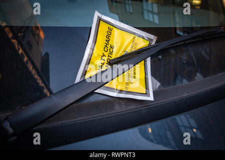 Yellow windscreen sticker containing a Fixed Penalty Parking Charge Notice for illegal parking fine fee stuck onto a car windscreen. Stock Photo