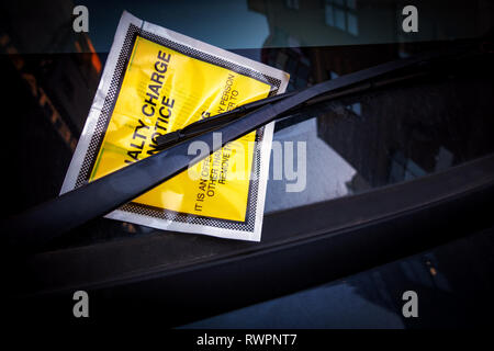 Yellow windscreen sticker containing a Fixed Penalty Parking Charge Notice for illegal parking fine fee stuck onto a car windscreen. Stock Photo