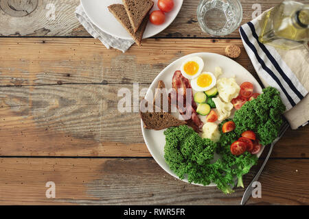 Plate of healthy food, breakfast or lunch top view. Cabbage kale, eggs, avocado, bacon, tomatoes, brussel sprouts, cauliflower bread toasts on wooden  Stock Photo