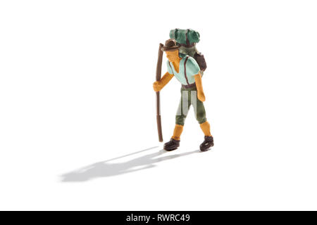 Miniature male backpacker with rucksack trekking on mountains with his hiking boots and stick isolated on white with shadow and copy space Stock Photo