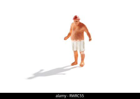 Obese miniature man with large fat paunch in bathing trunks standing on a beach isolated on white with shadow Stock Photo