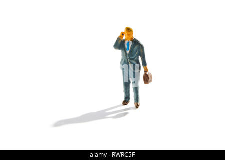 Miniature businessman with briefcase using a mobile phone having a conversation as he walks along with shadow on white Stock Photo
