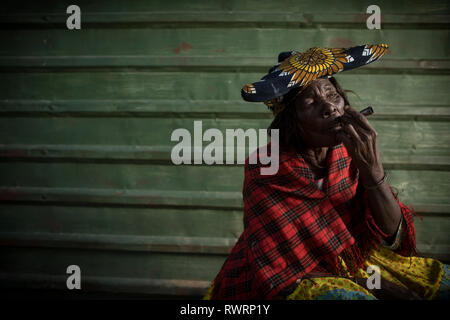 A Herero woman smoke outside a store in Purros, Namibia. Stock Photo