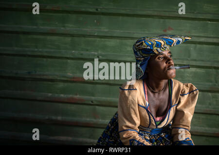 A Herero woman smoke outside a store in Purros, Namibia. Stock Photo